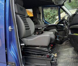 Interior of a blue truck cab with two gray seats and a raised driver's area, view from the open door, showing the dashboard and overhead console.