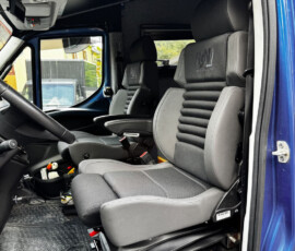 Interior of a blue truck cab showing the driver's seat, passenger seat, and overhead controls above the windshield area, with rubber floor mats.