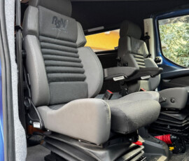 Interior of a blue truck/van cab showing two grey captain seats with ribbed backs, mounted on adjustable bases and ready for use, with tools on the floor nearby